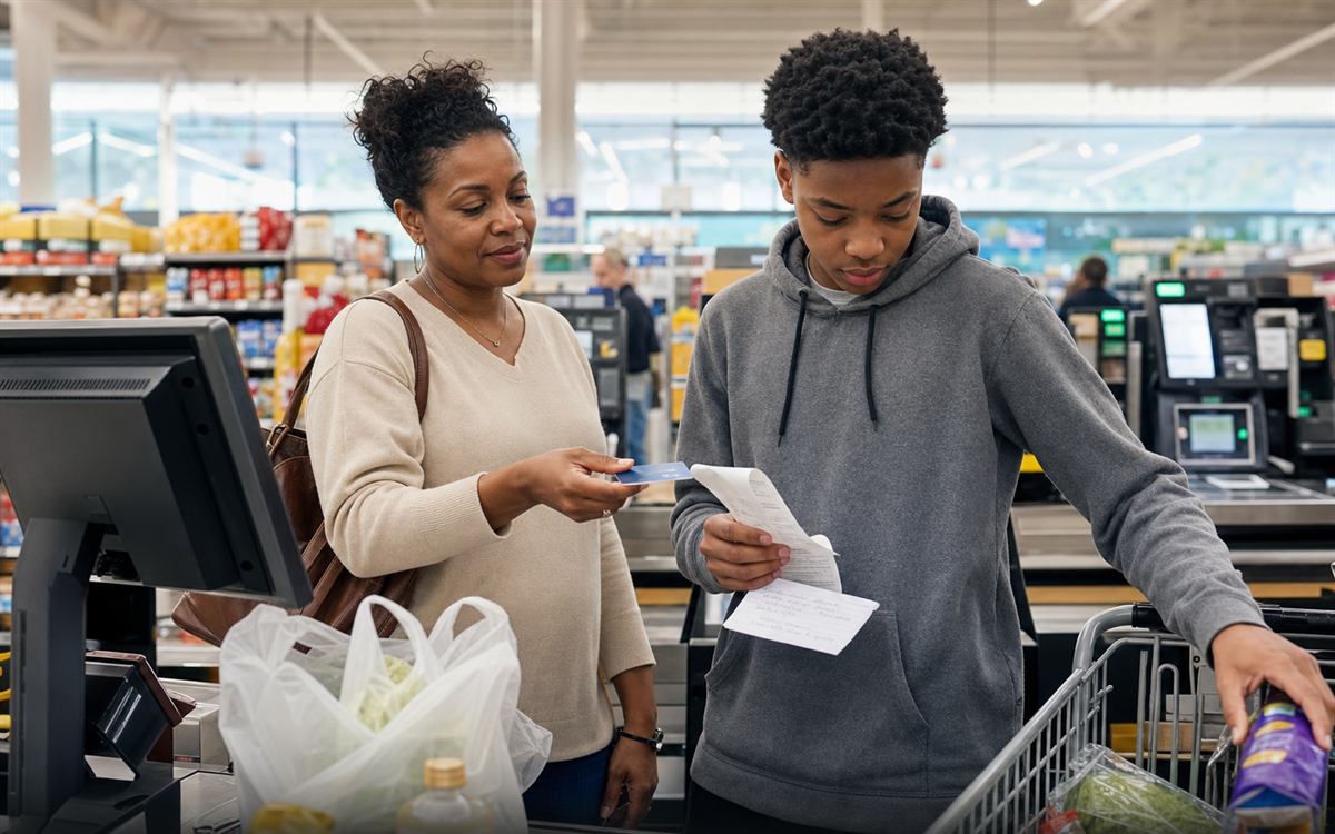 Illustrative scene of a parent handing her teen a payment card and receipt at a grocery checkout